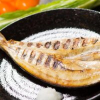 barred Spanish mackerel in a pan with fresh vegetables next it.