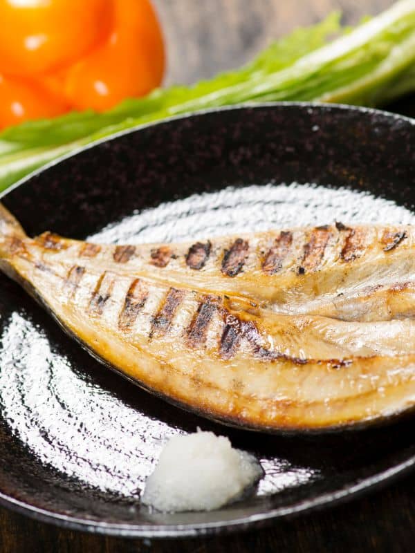barred Spanish mackerel in a pan with fresh vegetables next it.