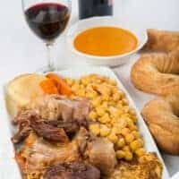 Cocido Madrileno on a plate served with a glass of red wine and bread