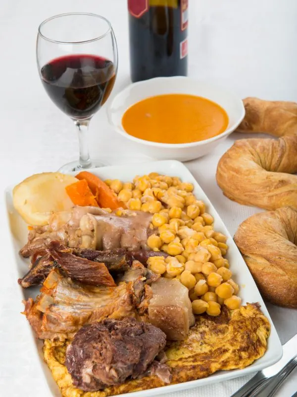 Cocido Madrileno on a plate served with a glass of red wine and bread