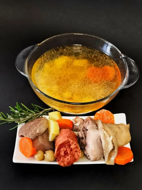 Cocido Madrileno served on a plate with a glass bowl of meat broth