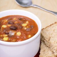 Spanish Black Bean And Corn Soup in a white bowl served with bread.