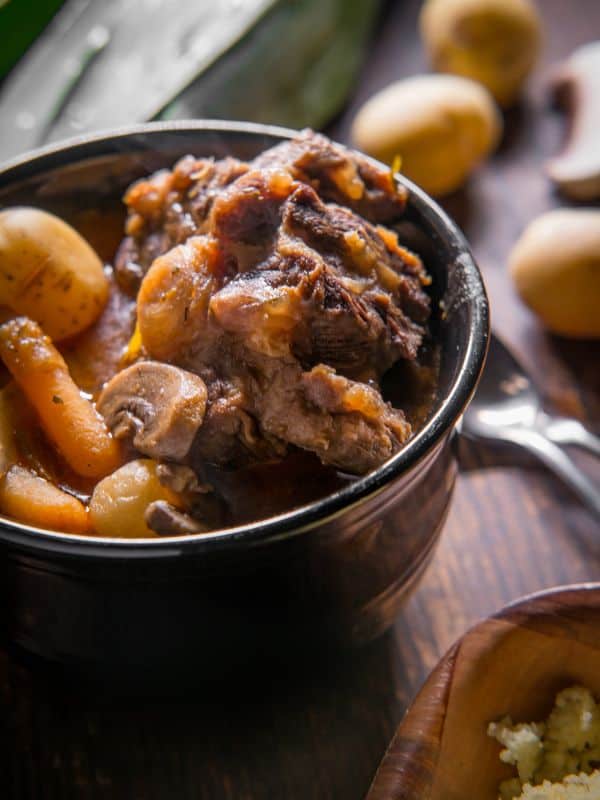 a bowl of oxtail stew with potatoes on a wooden table.