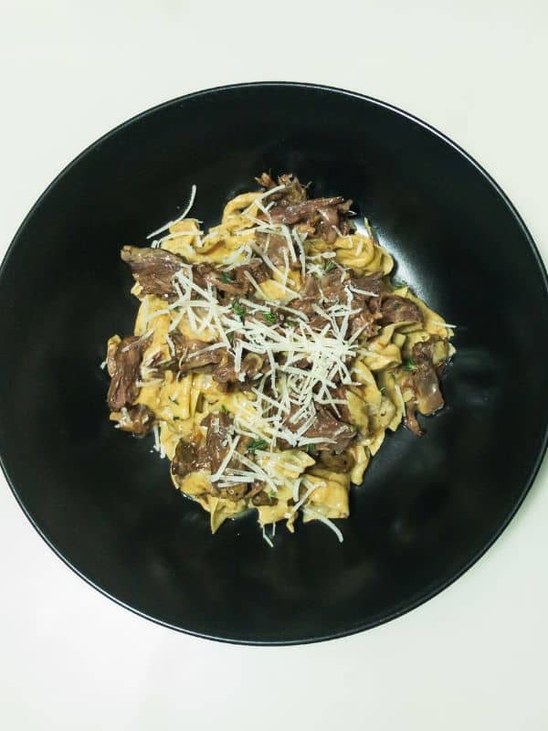 a plate containing oxtail pasta recipe with cheese on top