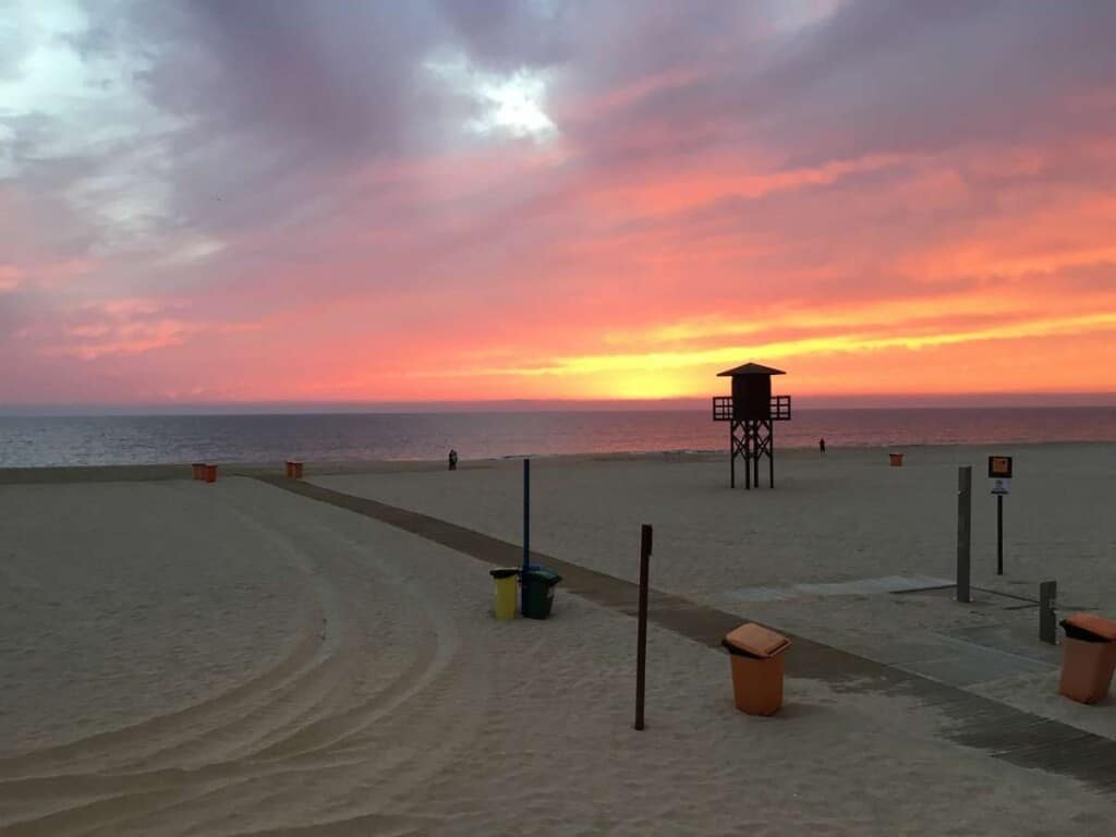 white sandy beach with a walkway and trash cans around as and a lifeguard house during a sunset