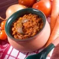 oxtail ragu recipe in a clay pot with vegetables next to it.