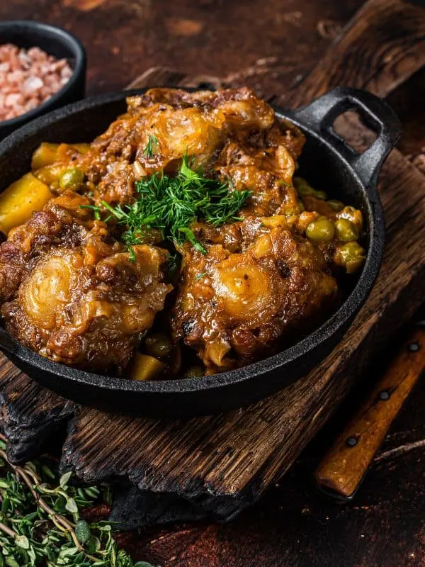 baked oxtails and gravy in a cast iron on a wooden table