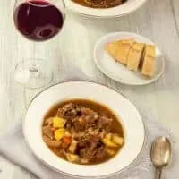rabo de toro stew in 2 bowls with a glass of red wine