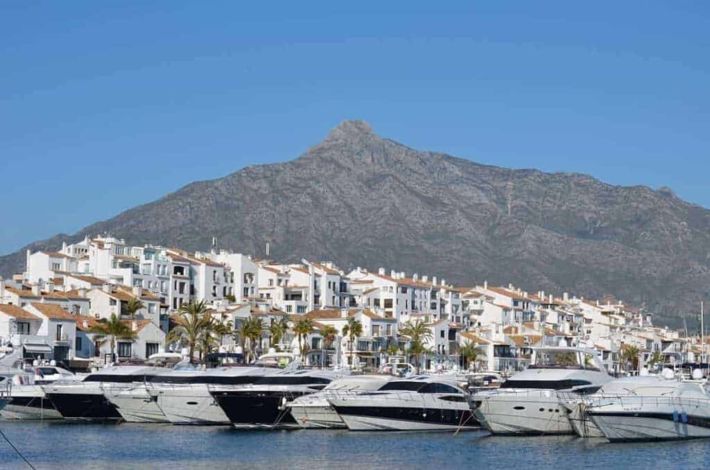 boats docked on a pier with a view of white buildings and houses and a mountain, where to stay in Andalusia