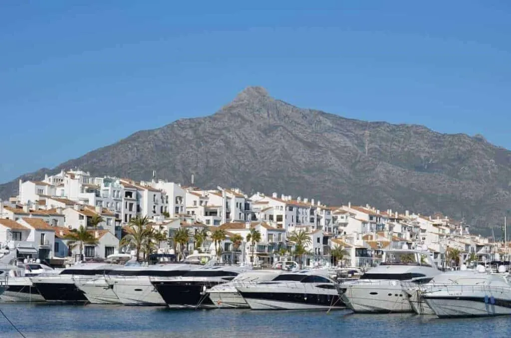 boats docked on a pier with a view of white buildings and houses and a mountain, where to stay in Andalusia