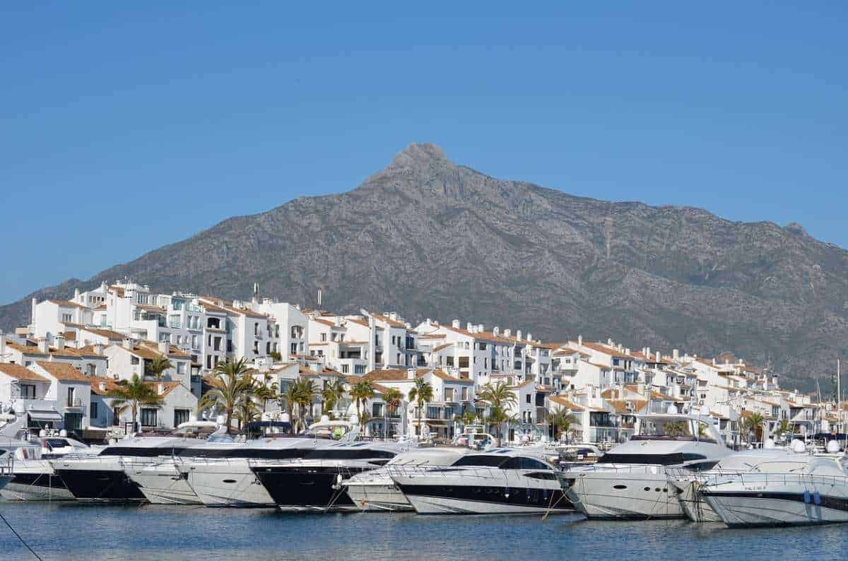 boats docked on a pier with a view of white buildings and houses and a mountain