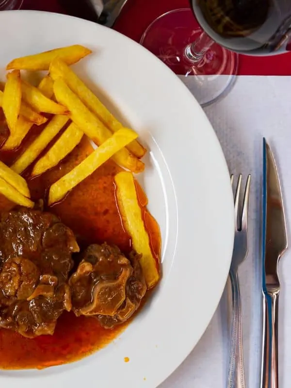 baked oxtails and gravy served with potato fries and a glass of red wine