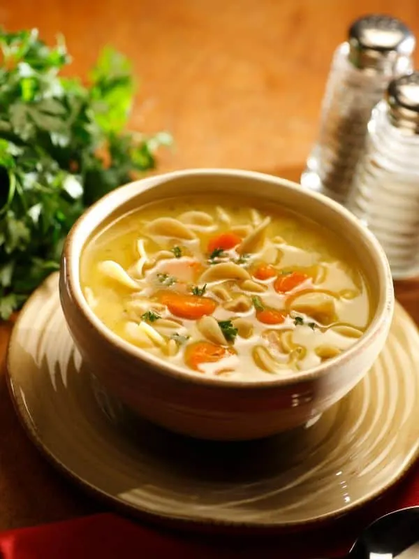 Gluten-Free Chicken Noodle Soup in a clay bowl with fresh parsley in the background