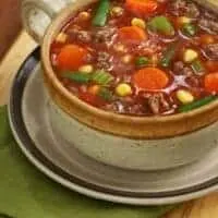 a bowl of oxtail vegetable soup on a wooden table on a green napkin