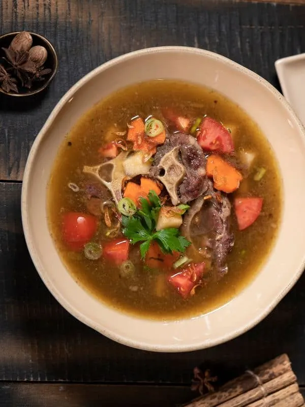 a bowl of oxtail vegetable soup on a wooden table