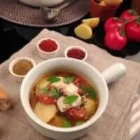 flounder soup in a cup with tomatoes, spices and garlic next to it