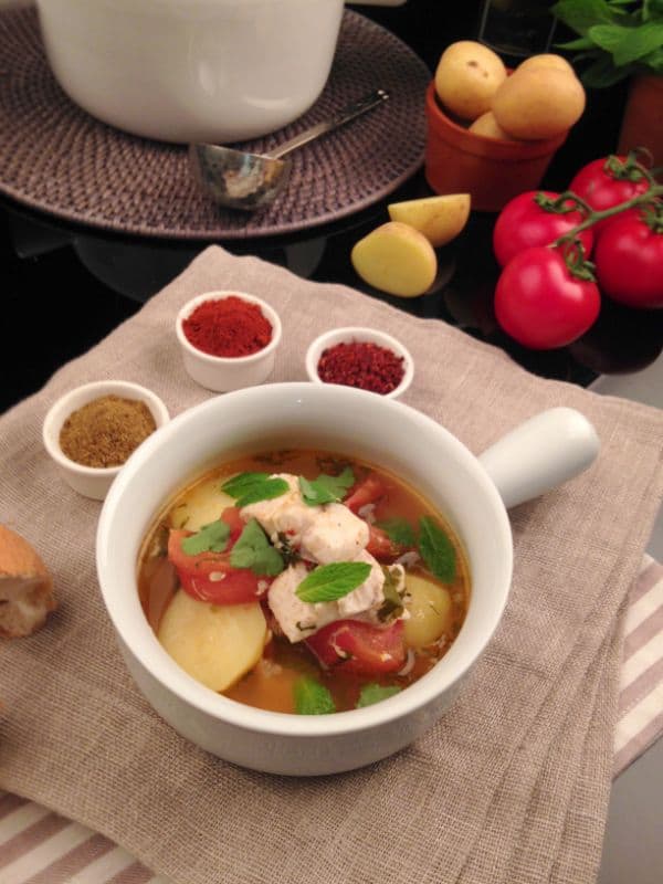 flounder soup in a cup with tomatoes, spices and garlic next to it