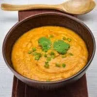 Orange Lentil Soup in a wooden bowl on a napkin with a wooden spoon next to it