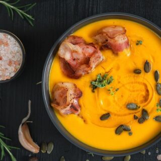 pumpkin chorizo soup in a black bowl with serrano ham and seeds on top
