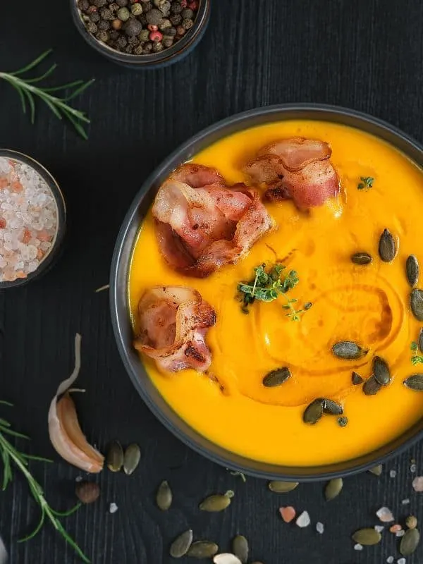 pumpkin and sweet potato soup from Spain in a black bowl with serrano ham and seeds on top