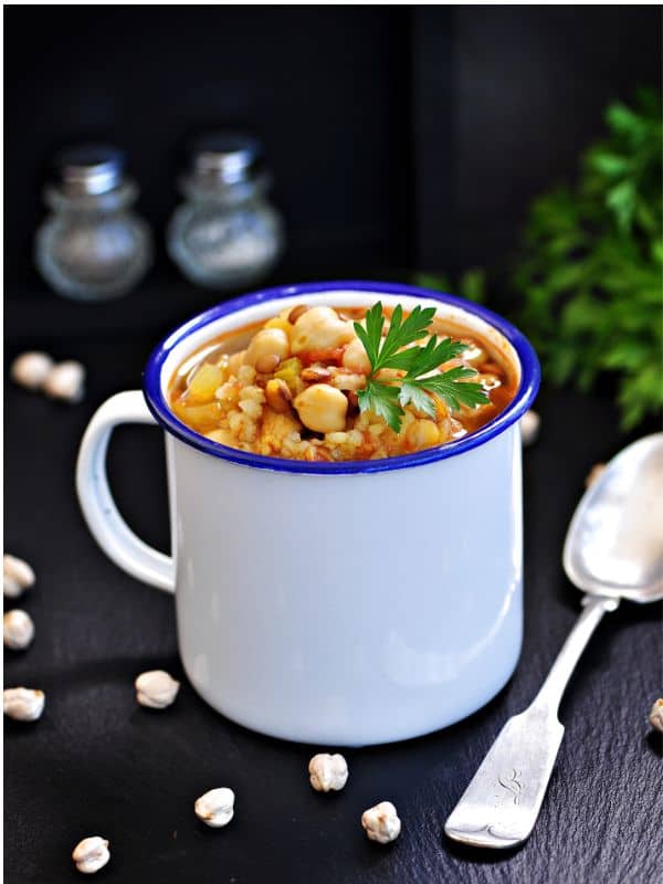 a cup with spanish soup with chickpeas on a black surface