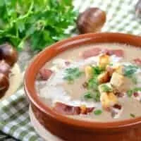 Chestnut And Chorizo Soup in a clay bowl with chestnuts next to it