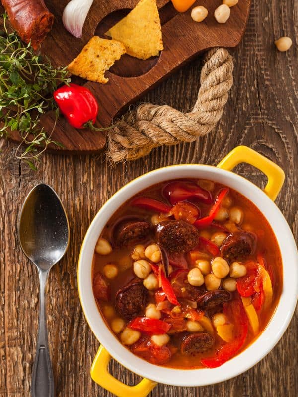 garbanzo bean soup with chorizo in a yellow clay bowl on a wooden table