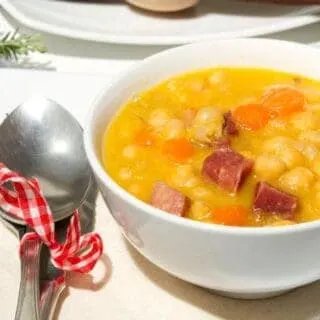 garbanzo bean soup with ham in a bowl with a spoon next to it.