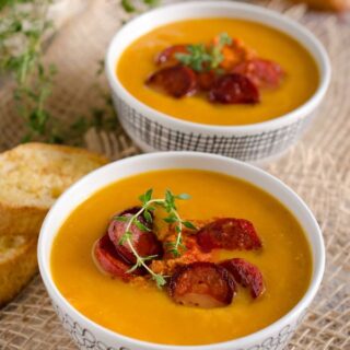 pumpkin chorizo soup in 2 bowls with some slices of bread next to them