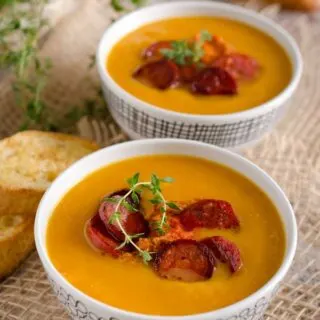 pumpkin chorizo soup in 2 bowls with some slices of bread next to them