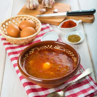 spanish garlic and bread soup in a clay bowl with eggs and other ingredients next to it.