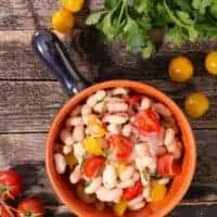 warm cannellini bean salad in a pot on a wooden table with fresh cherry tomatoes next to it