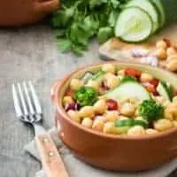 chickpea and chorizo salad in 2 clay bowls with a cucumber and parsley next to it