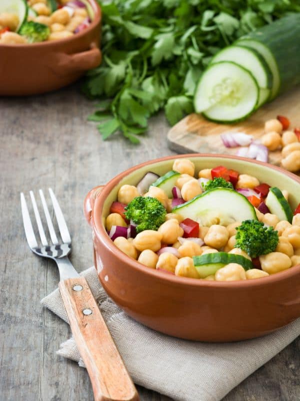 chickpea and chorizo salad in 2 clay bowls with a cucumber and parsley next to it