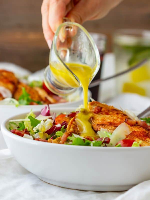 chicken bacon salad in a bowl with a cup of sauce being poured over it.