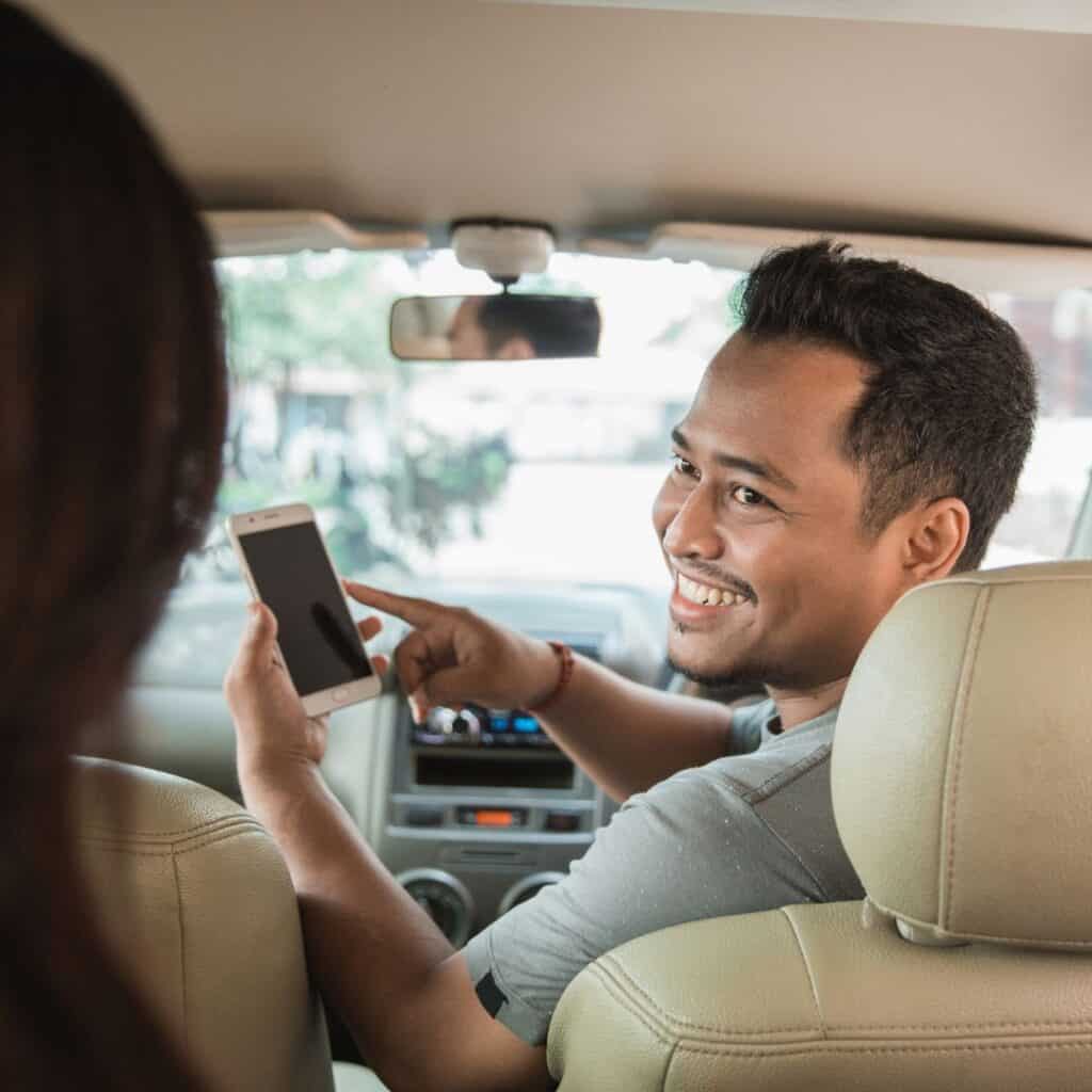 a person on the front of car seat pointing to his phone while talking to a woman at the back seat