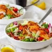 crispy chicken salad in 2 bowls with a glass of dressing next to them