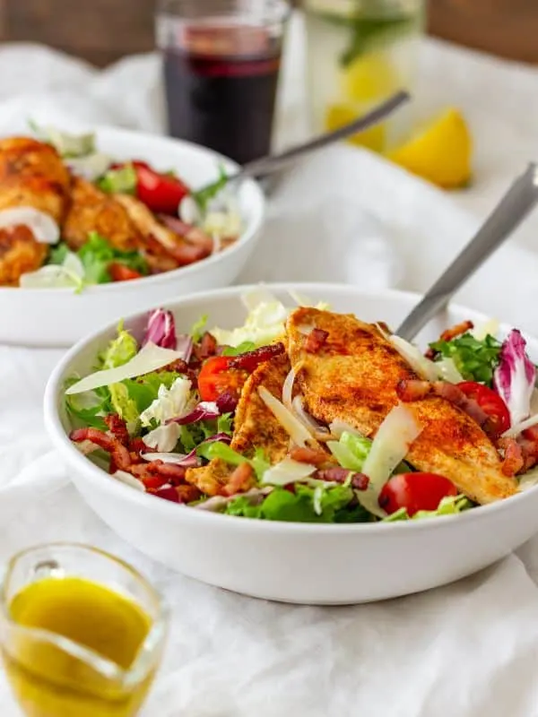 chicken bacon salad in 2 bowls with a glass of dressing next to them