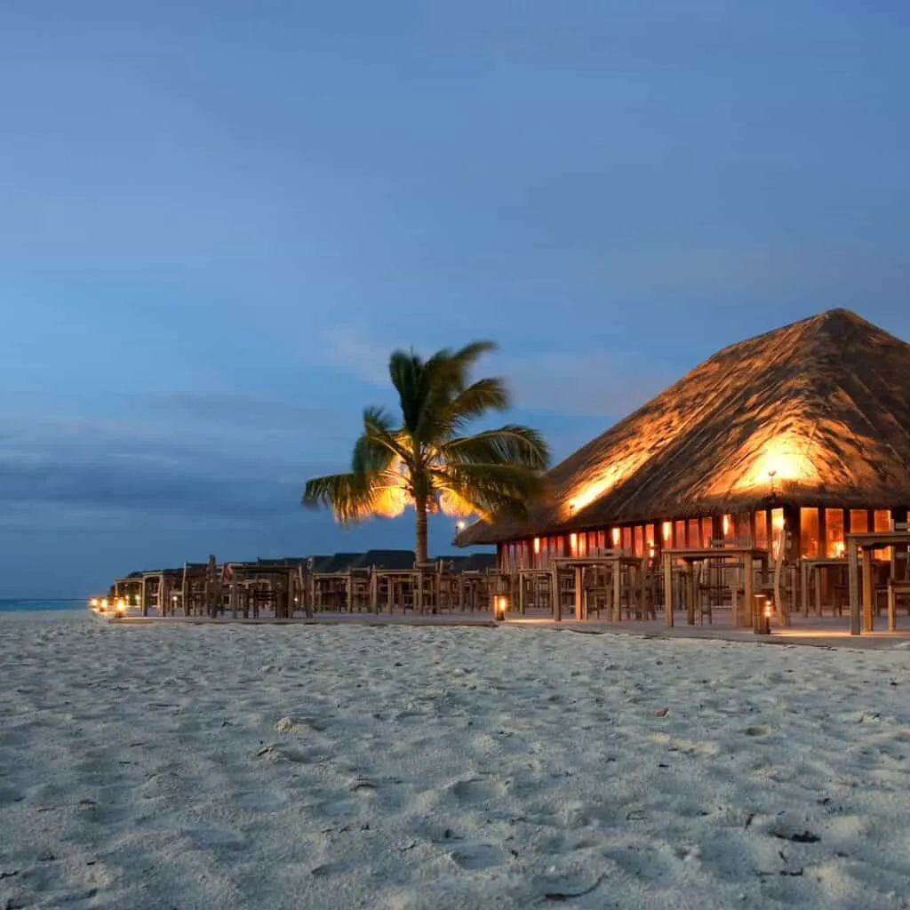 a beach with thatched huts and palm trees at dusk