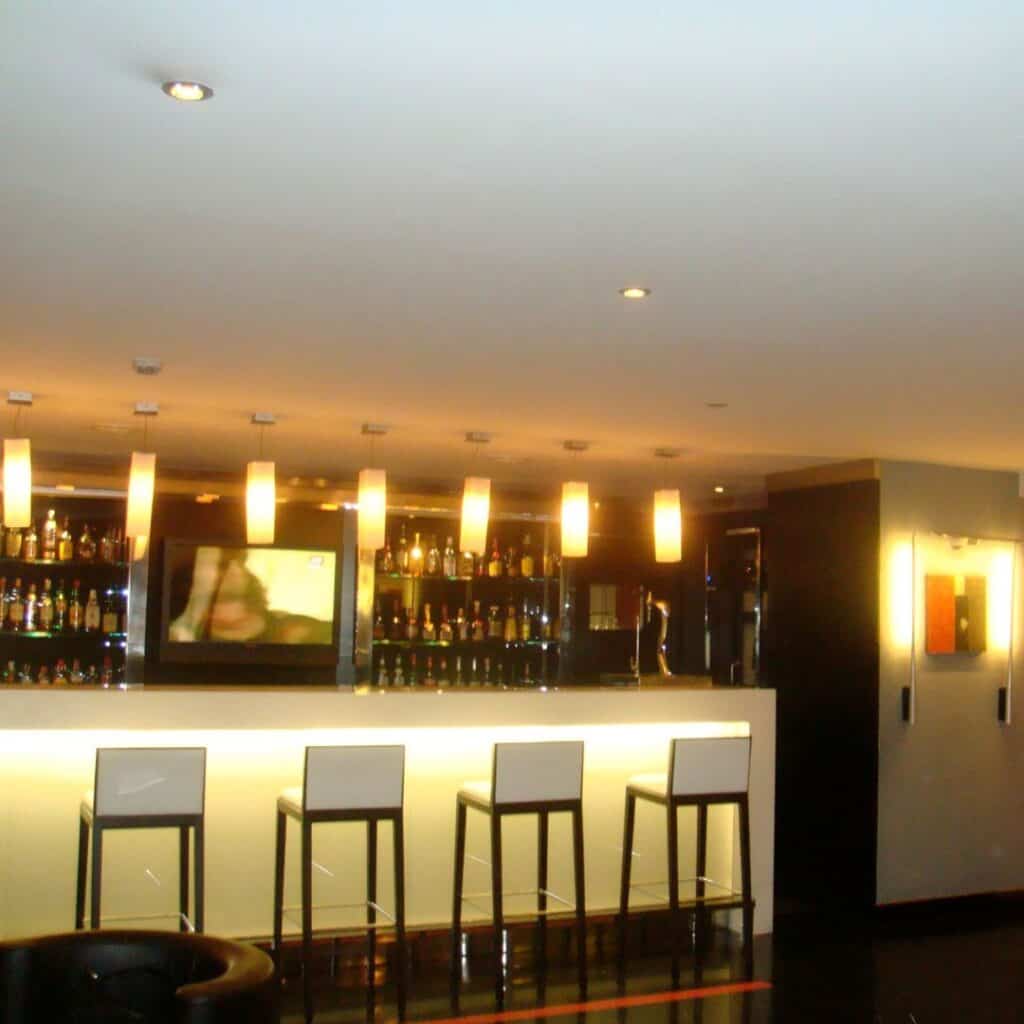 a bar with several stools and a television on the wall with yellow lights