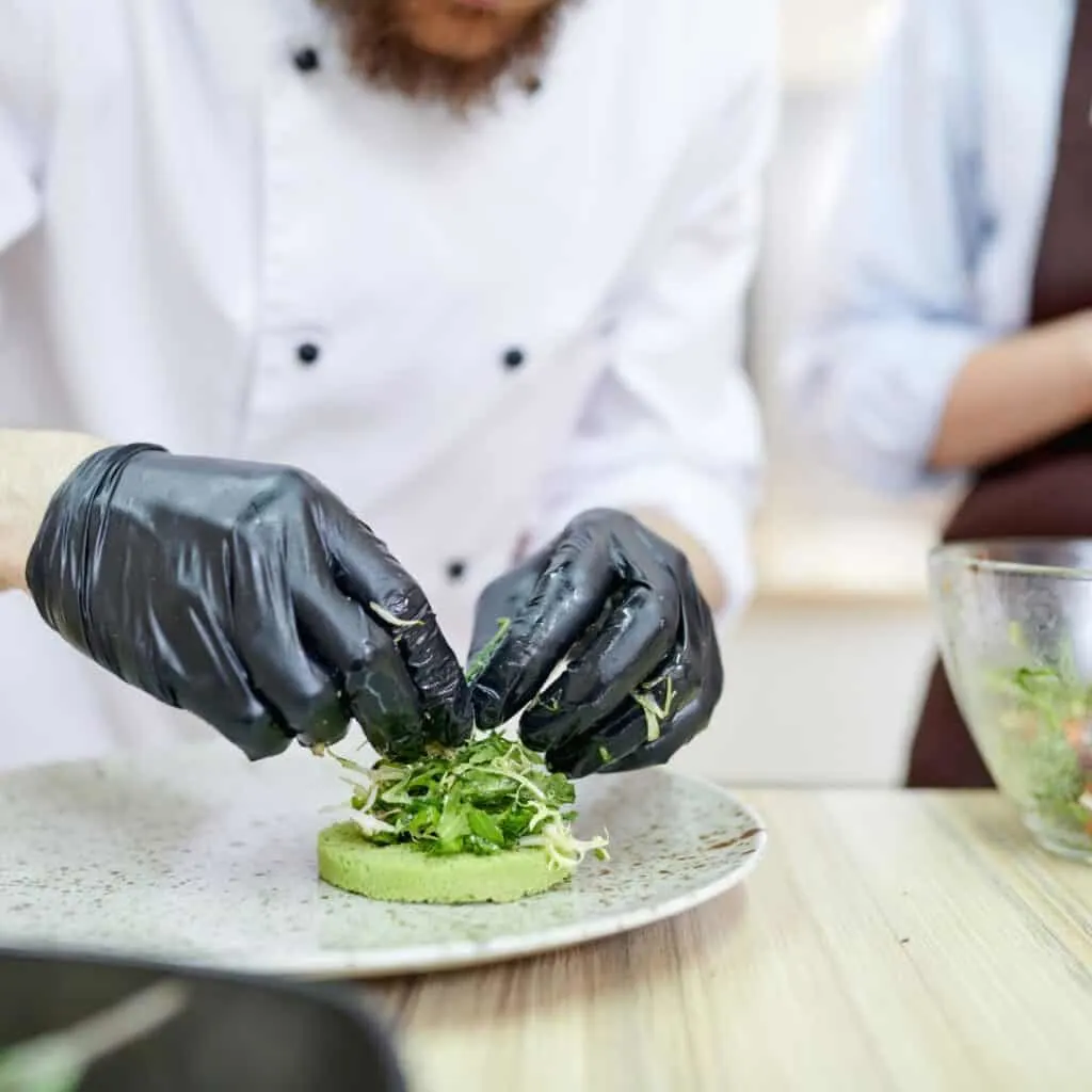 a person in a chef's hat and gloves preparing food on a plate