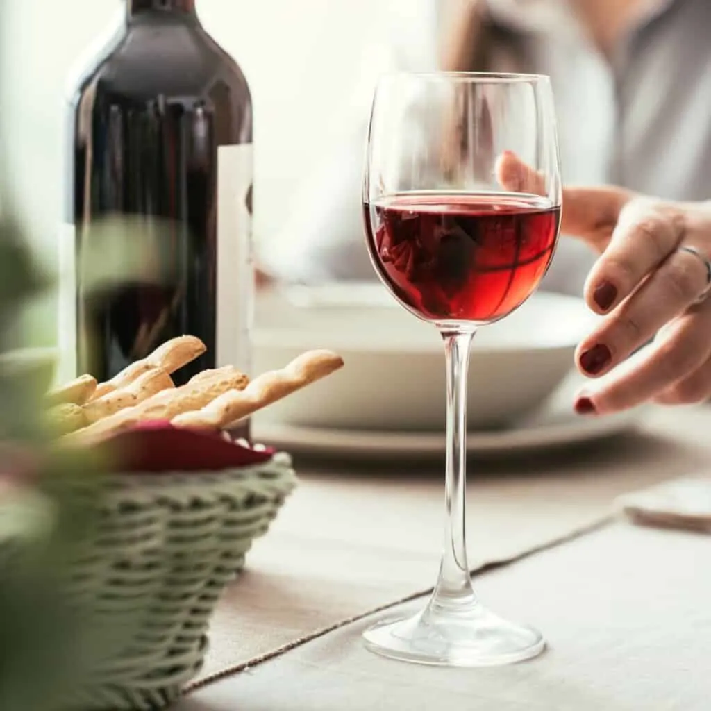 A person holding a glass of red wine while sitting at a table