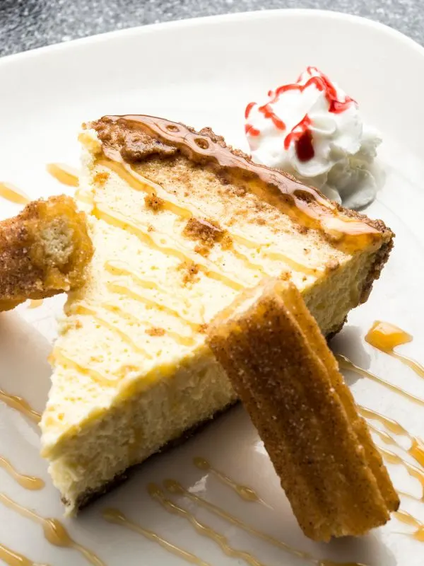 slice of churros cheesecake on a place served with whipped cream