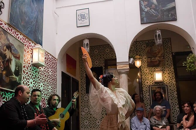 inside a casa with a flamenco dancer raising her fan with guitarists and audience on the side