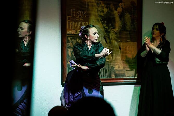 a woman in black dancing flamenco on stage with a frame at the back with a woman clapping by her side