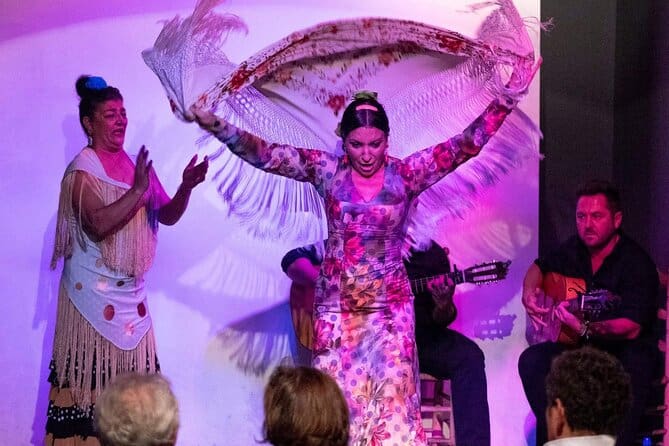 a woman dancing flamenco with her shawl, a woamn clapping on the side and two guitarists