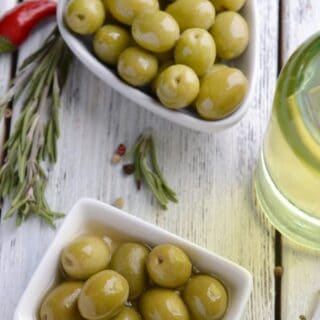 spanish marinated olives in 2 bowls with rosemary and chilli next to them