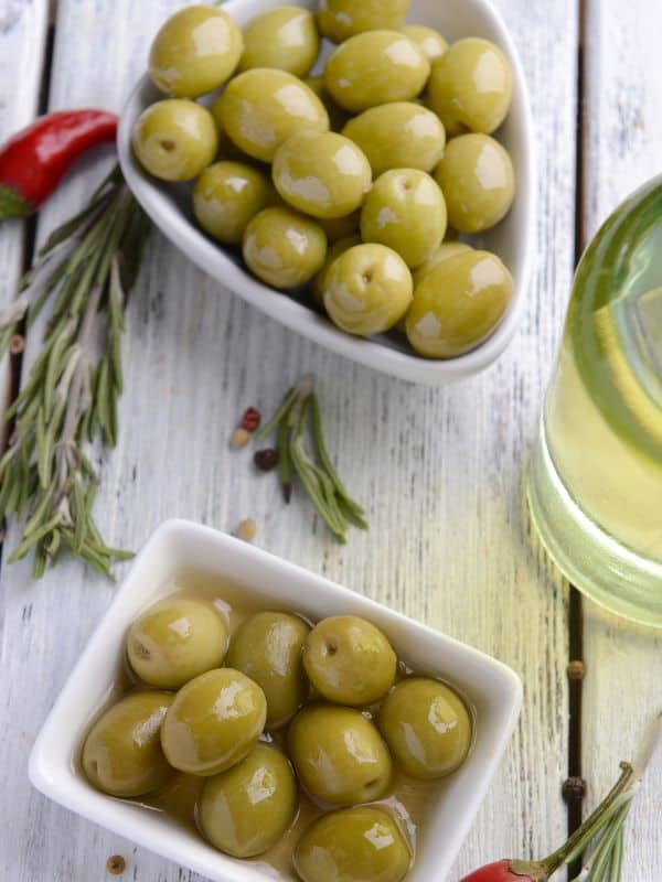 spanish marinated olives in 2 bowls with rosemary and chilli next to them
