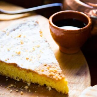 a slice of tarta de santiago on a wooden board with a drink next to it