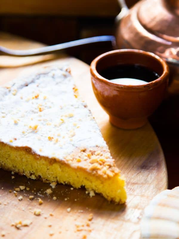 a slice of tarta de santiago on a wooden board with a drink next to it